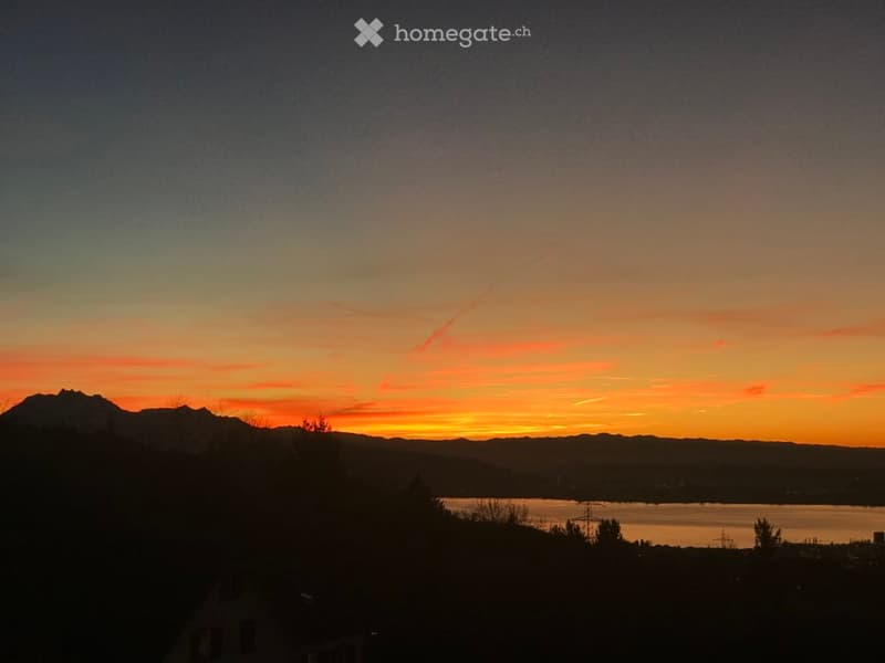 A serene view of a sunset over a lake with mountains in the background, showcasing a tranquil natural landscape.