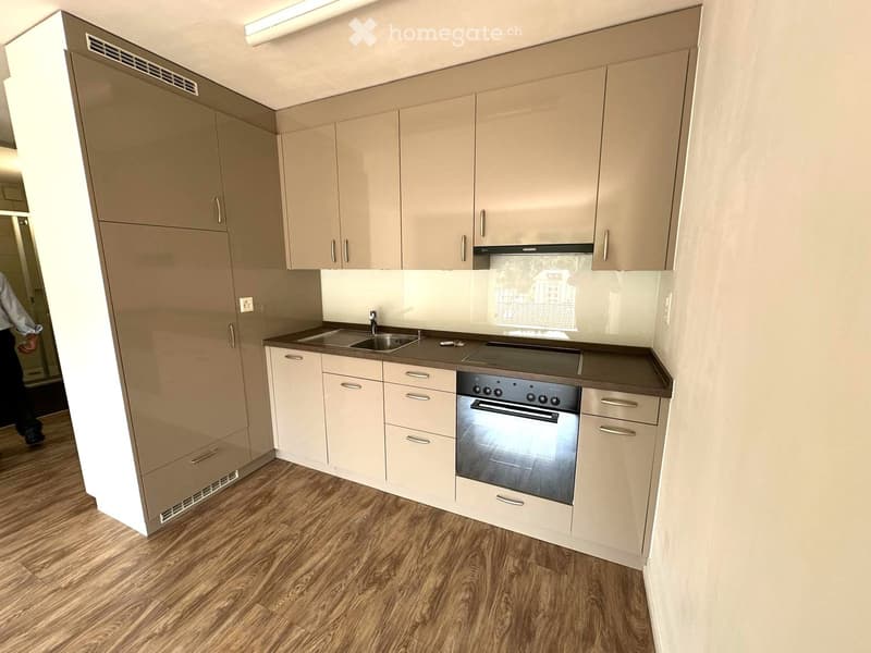 Modern kitchen with light-colored cabinets, a stainless steel oven, and a sink, featuring wooden flooring and ample storage space.