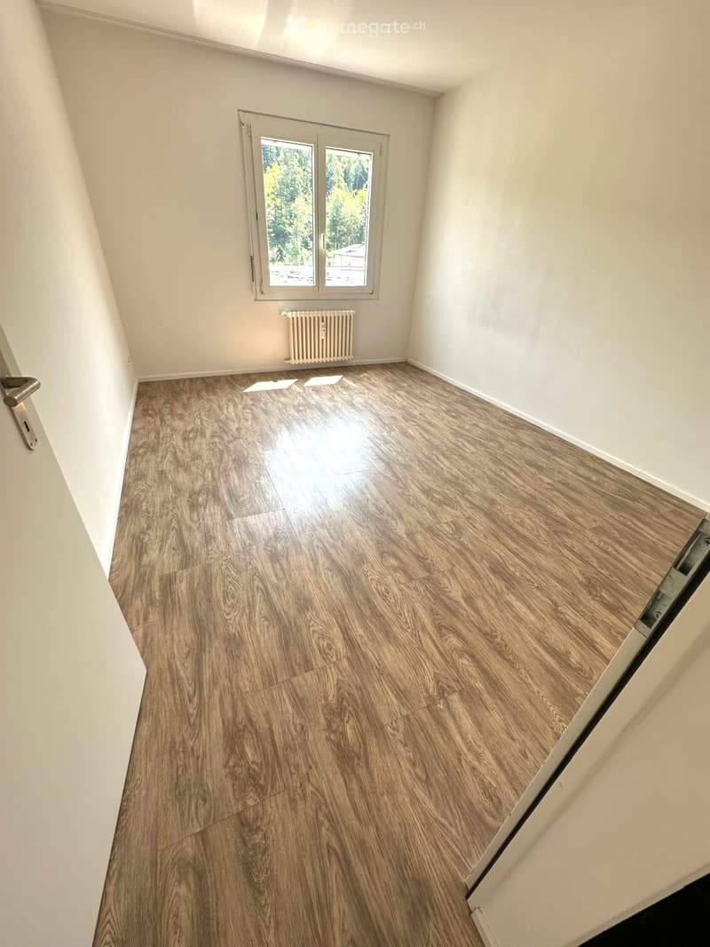 Empty room with wooden flooring, white walls, and a window with a radiator below it.