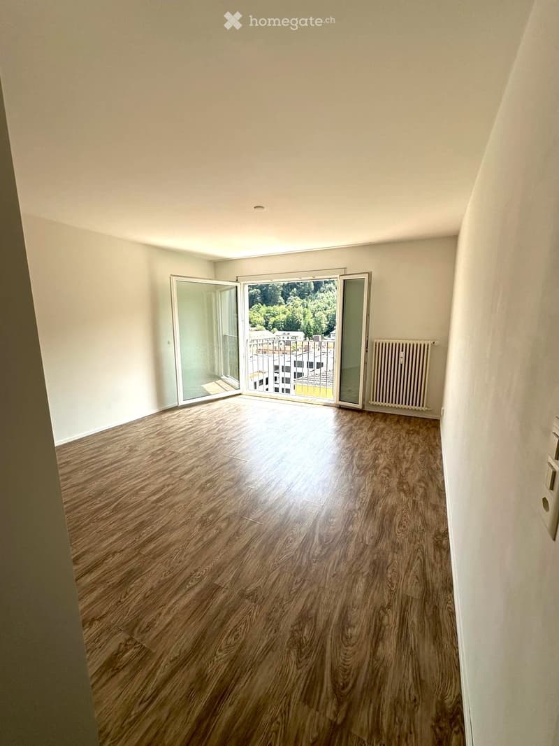 Empty room with wooden flooring, white walls, and large sliding glass doors leading to a balcony.