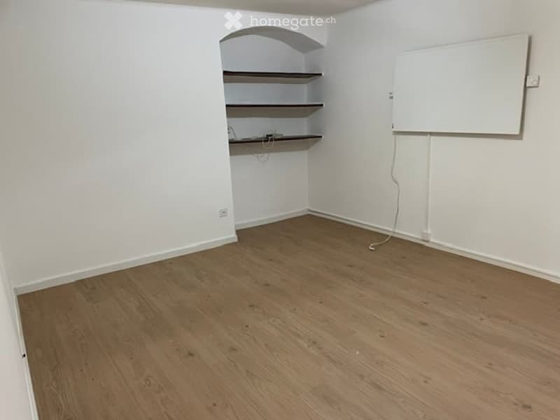 Empty room with wooden flooring, white walls, built-in shelving unit, and a whiteboard on the wall.