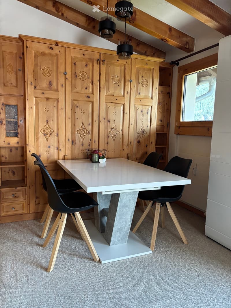 A modern dining area with a white table, four black chairs, wooden cabinets, and pendant lights.