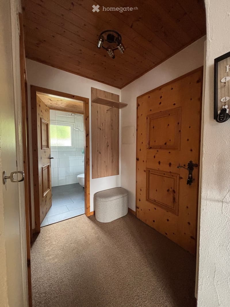 Carpeted hallway with wooden doors, a small wooden shelf, and a toilet visible through an open door.