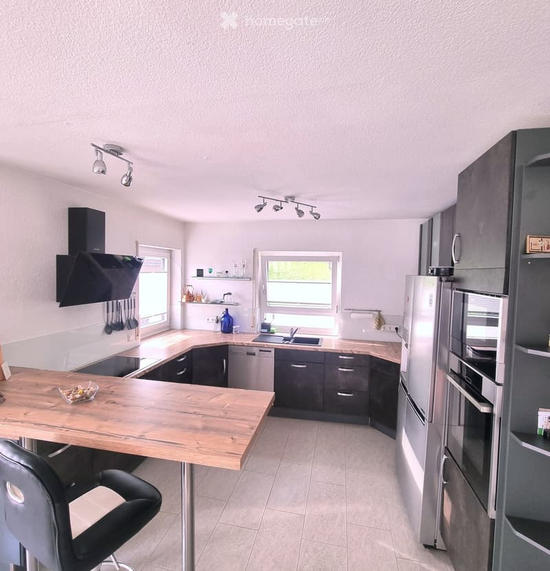 Modern kitchen with grey cabinets, wooden island, stainless steel appliances, and a black chair.