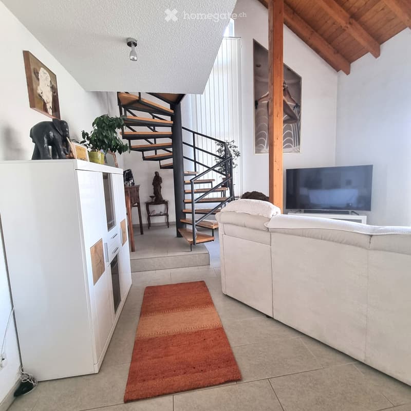 Modern living room with a white sofa, television, refrigerator, small wooden table, and decorative items including a plant and artwork.