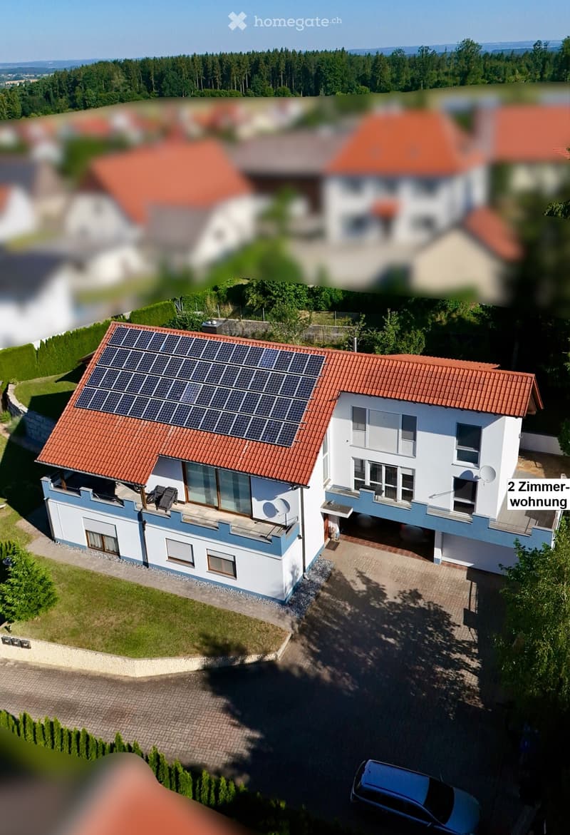 A two-story house with a red-tiled roof, solar panels on the roof, white and blue exterior, multiple windows, and a driveway with a parked car.