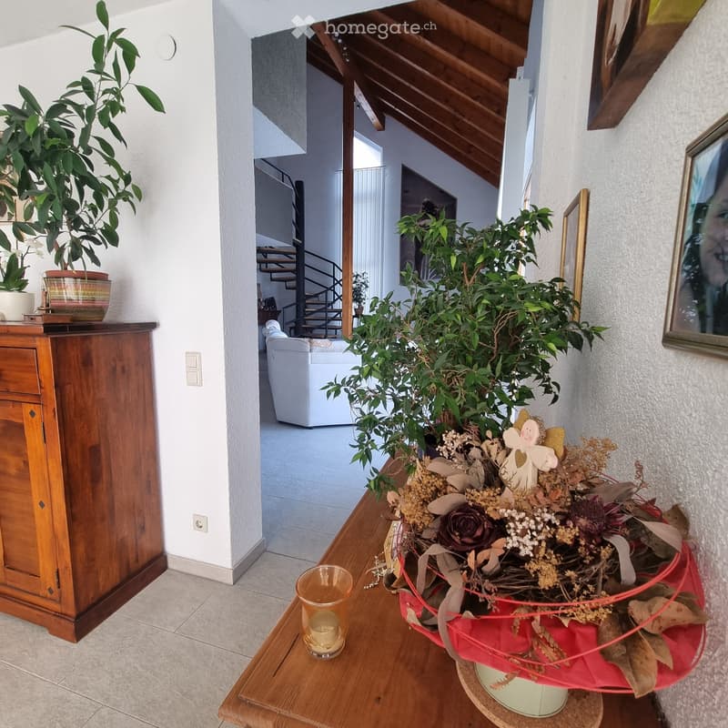 A well-lit hallway with a wooden table holding a candle and a decorative plant arrangement, leading to a living area with a white sofa and staircase.