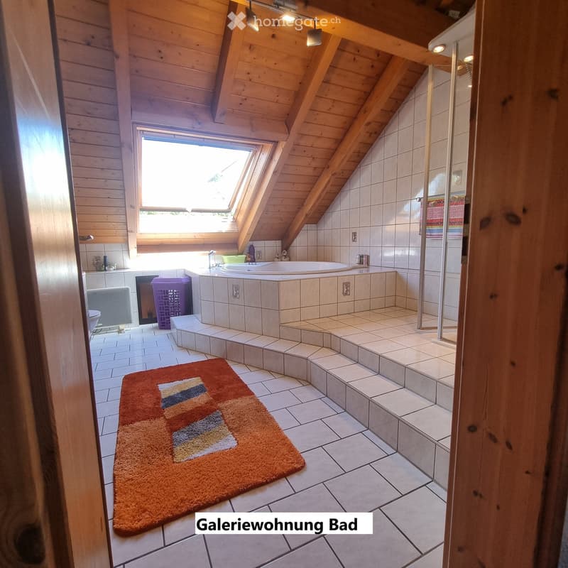 Bathroom with wooden ceiling beams, skylight window, tiled walls, bathtub, sink, shower, and a colorful bathroom rug.