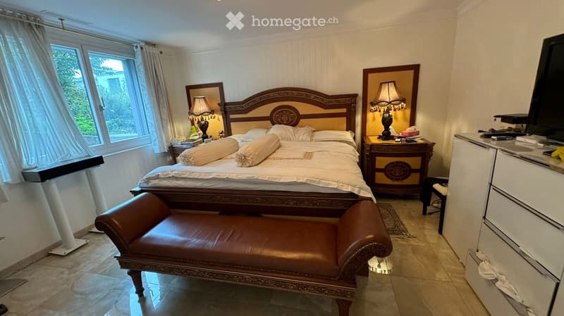 Elegant bedroom with a large wooden bed, nightstands with lamps, a leather bench, and a TV on a stand.