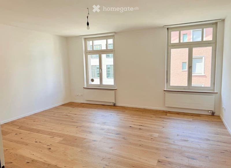 Empty room with wooden flooring, white walls, and large windows with radiators underneath. No furniture or equipment present.