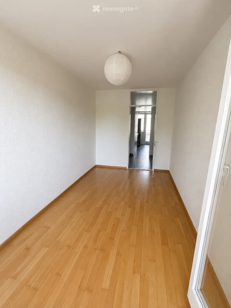 Empty hallway with light wooden flooring, white walls, and a spherical pendant light fixture.