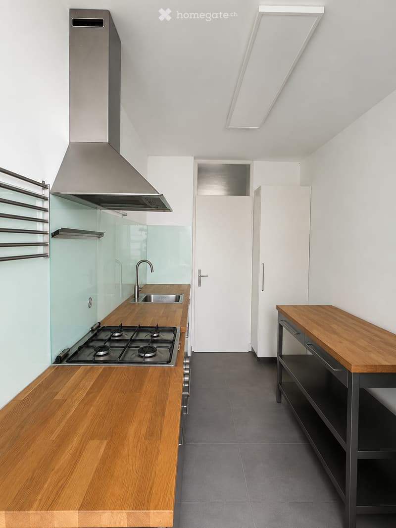 Modern kitchen with wooden countertops, stainless steel stove, sink, and faucet, white cabinets, and a glass shower enclosure.