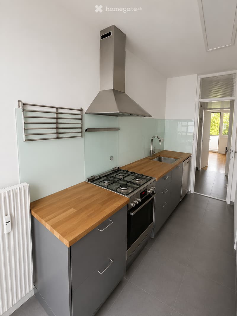 Modern kitchen with wooden countertops, stainless steel appliances, and dark grey cabinets. Features a gas stove, oven, sink, and a towel rack on the wall.