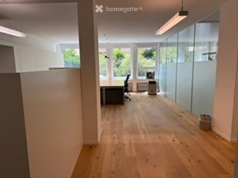 Bright, open-plan office space with wooden flooring, large windows, and glass partitions. Minimal furnishings, no major furniture or equipment visible.