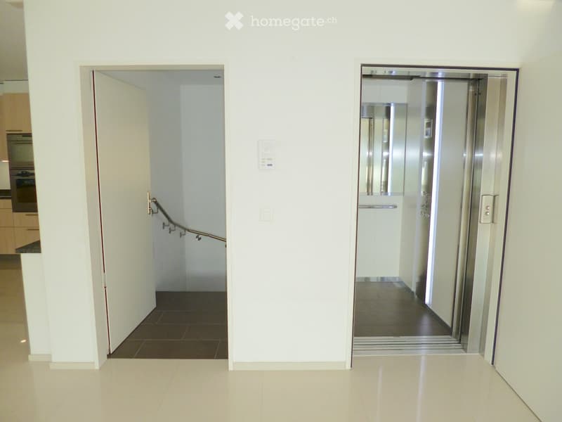 Modern hallway with white walls, tiled floors, and an elevator on the right and a staircase on the left.