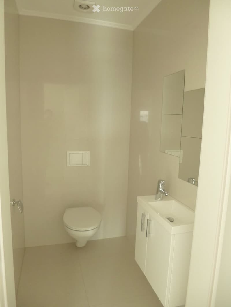 Modern, minimalist bathroom with beige tiles, a toilet, a sink with a mirror, and a white cabinet.