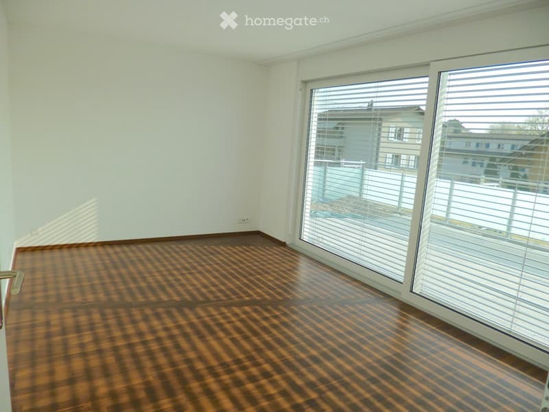 Empty room with wooden flooring and large windows with blinds, allowing natural light to fill the space.