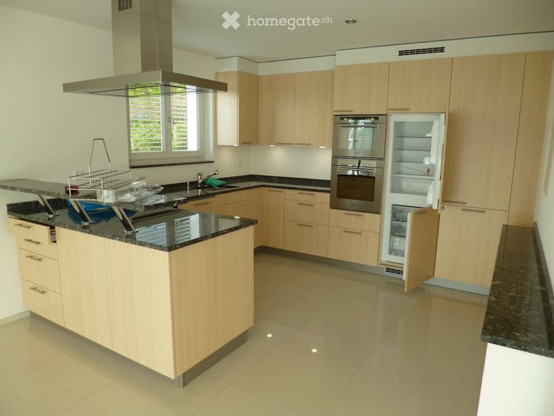 Modern kitchen with light wood cabinets, granite countertops, stainless steel appliances, and a central island.