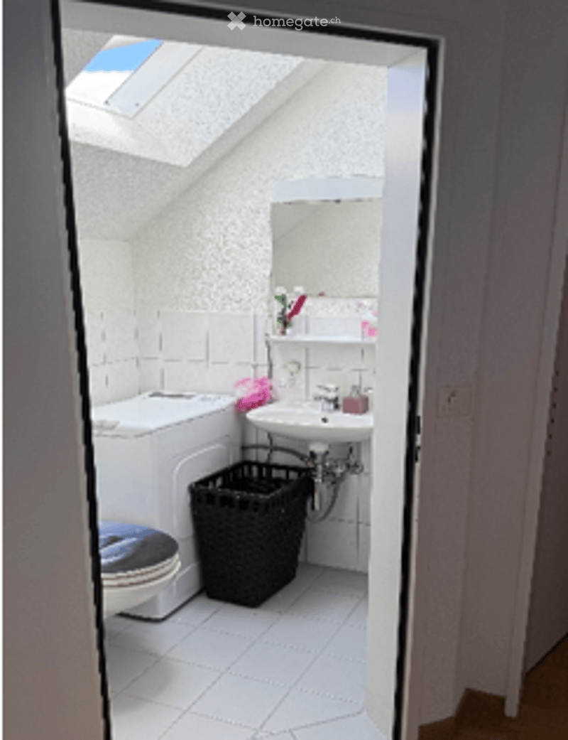 Small bathroom with white tiled floor, toilet, sink, mirror, and a wicker basket on the floor.