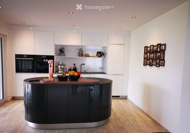 Modern kitchen with white cabinets, black island, stainless steel appliances, and a display of framed photos on the wall.