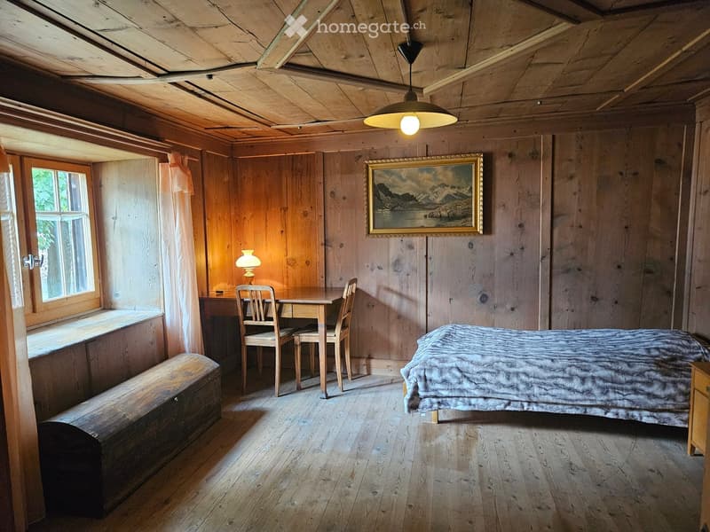 Cozy wooden bedroom with a bed, small table, chairs, a bench, and a painting on the wall.