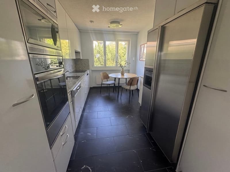 Modern kitchen with white cabinets, stainless steel appliances, dark tiled floor, and a small dining area with a round table and chairs.