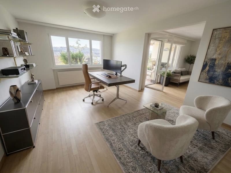 Modern, well-lit room with wooden flooring, large windows offering a scenic view, an office area with a desk and chair, a sitting area with armchairs and a coffee table, and a cabinet with decorative items.
