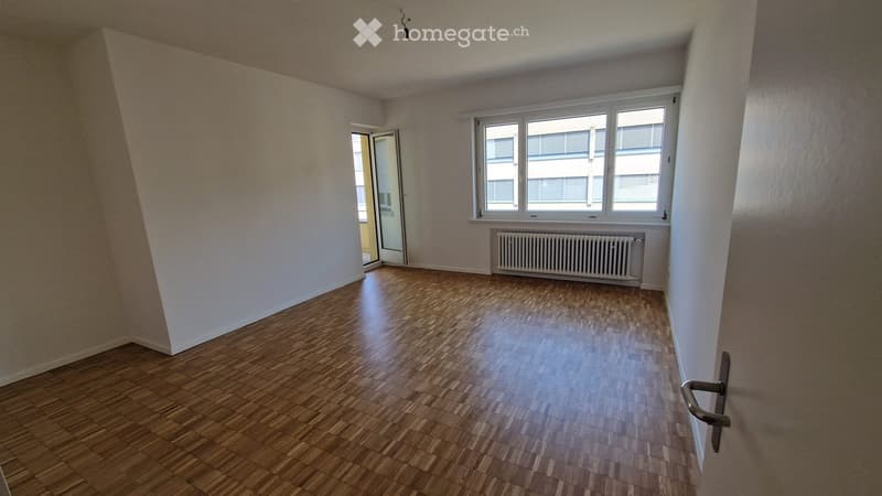 Empty room with wooden flooring, white walls, large windows, and a radiator. No furniture or equipment present.