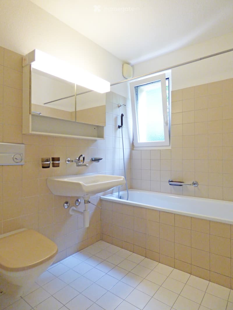 Bathroom with a white sink, bathtub, toilet, mirror, and a window letting in natural light.