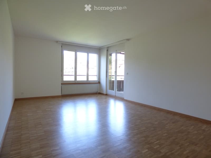 Empty room with wooden flooring, white walls, large windows, and a radiator. No furniture or equipment present.