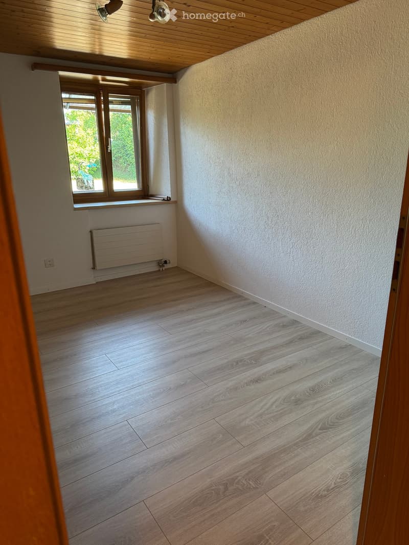 Empty room with wooden flooring, white walls, a window with wooden frame, and a radiator under the window.