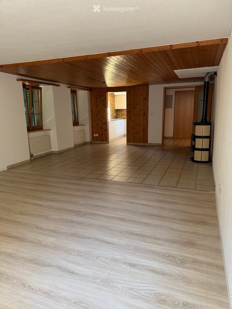 Empty room with wooden flooring and white walls, featuring a wooden ceiling and a tiled area in the background.