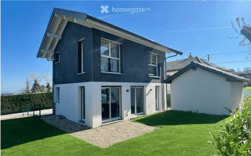 Modern two-story house with dark grey and white exterior, large windows, and a spacious front yard with artificial grass and gravel pathway.
