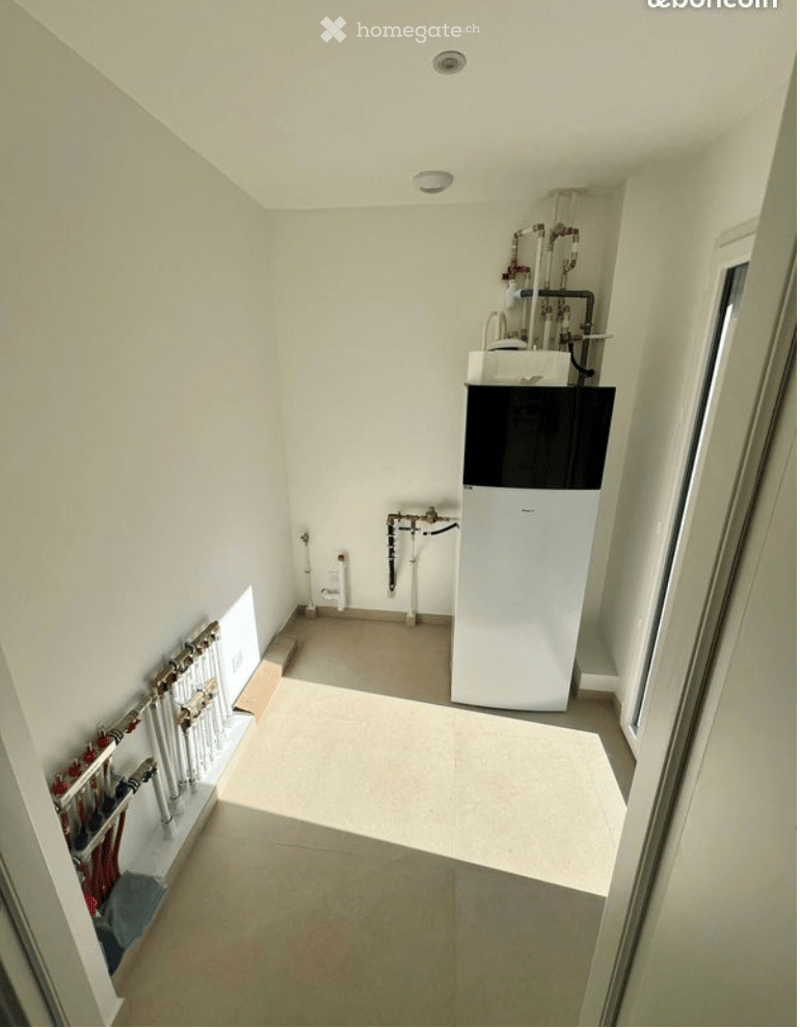 Utility room with white walls, tiled floor, and various pipes and appliances including a water heater and a refrigerator.