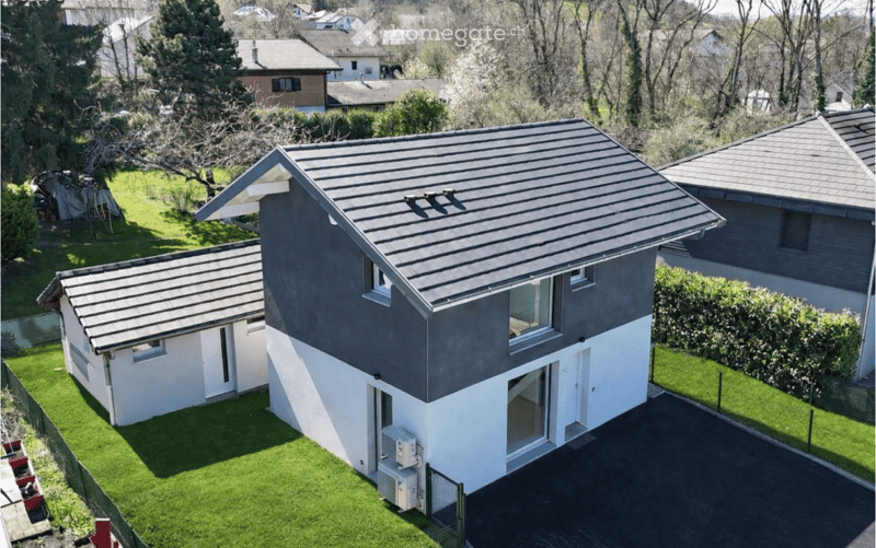 A modern two-story house with a grey metal roof and white lower facade, surrounded by a well-maintained lawn and neighboring houses.