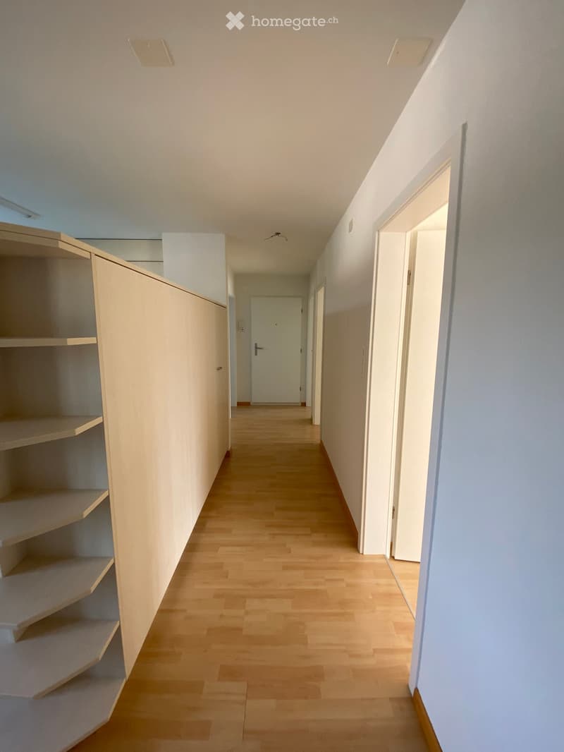 Empty hallway with wooden floor, white walls, and shelves