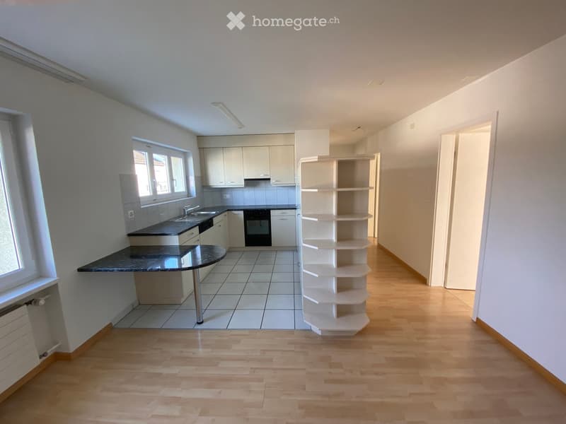 Modern kitchen with a central island, white kitchen cabinets, black countertops, white tiled floor, white shelving, underfloor heating, and a glass window with blinds.