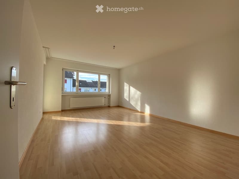 Empty room with wooden floor, white walls, a window with a view, and an open door leading to the hallway.