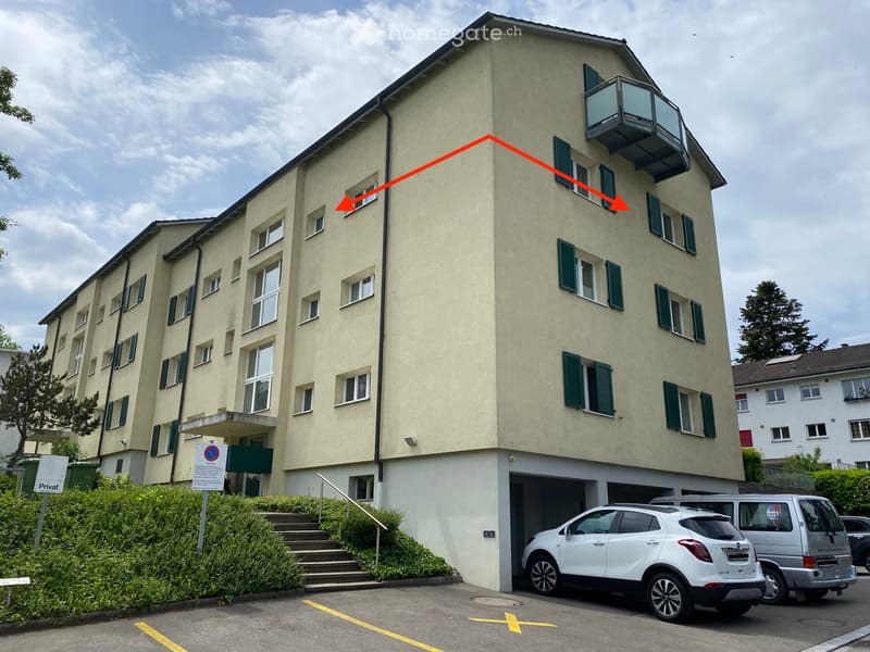 Large apartment building with multiple floors, green windows, balcony, attached garage, and parking spots.