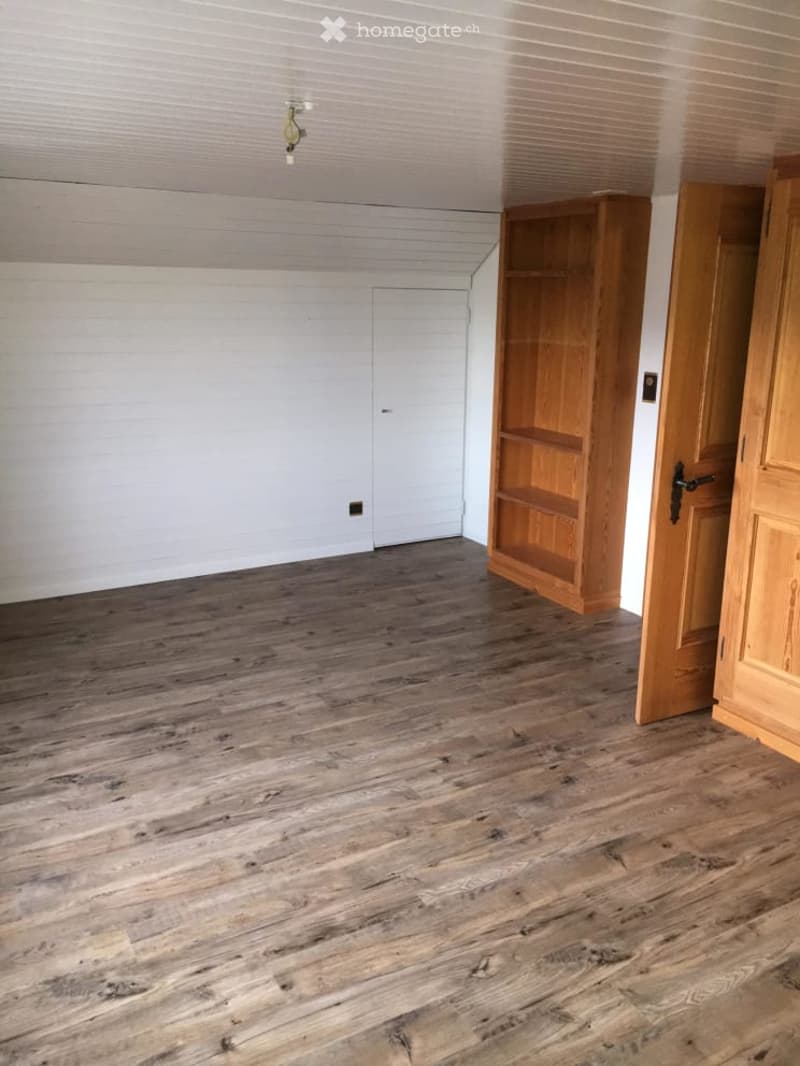 Empty room with wooden flooring, white walls, and a built-in wooden shelf unit.