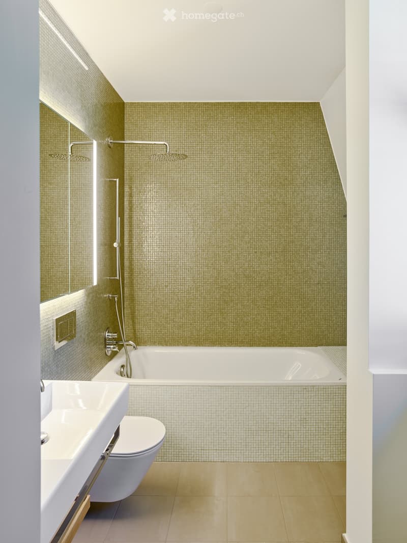Modern bathroom with a bathtub, toilet, sink, and showerhead. Green mosaic tiles on the walls and light-colored tiles on the floor.