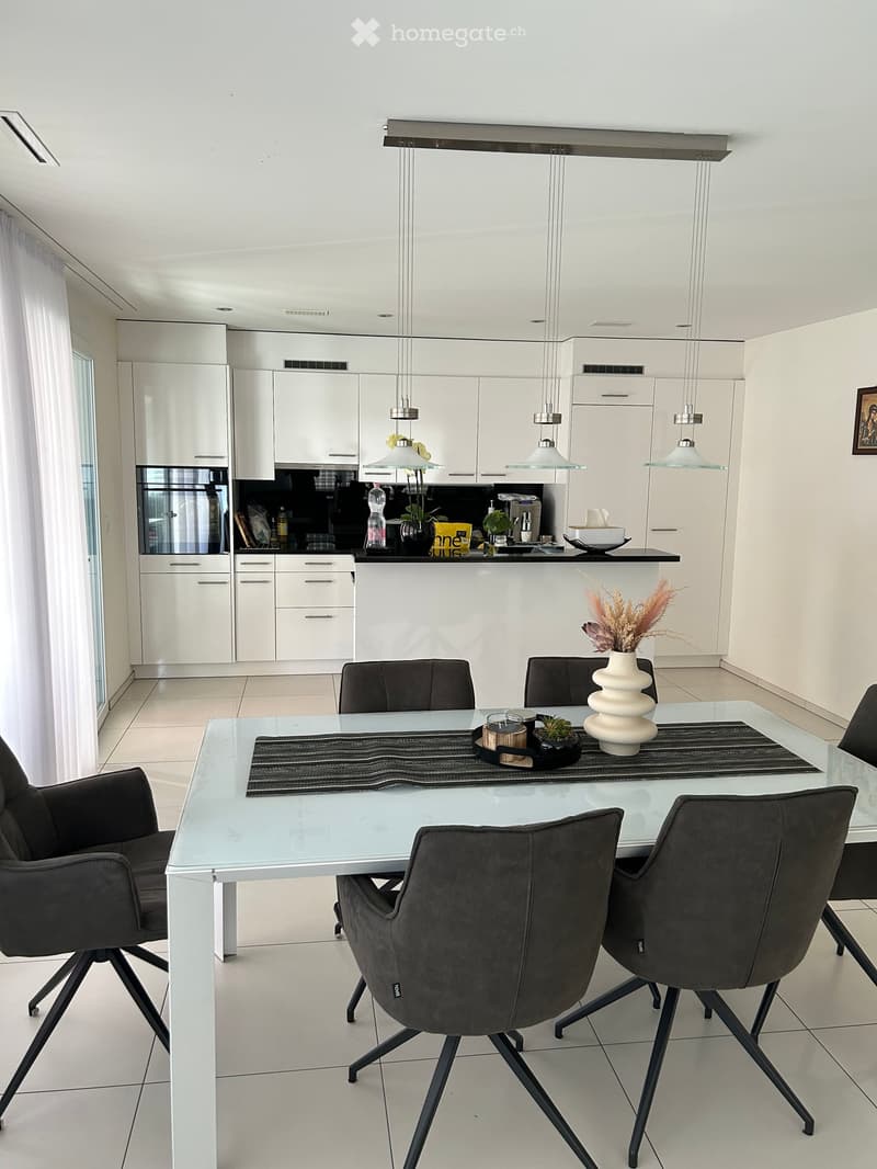 Modern kitchen with white cabinets, a glass dining table surrounded by black chairs, and a kitchen island with various items including a vase, bowl, and bottle.