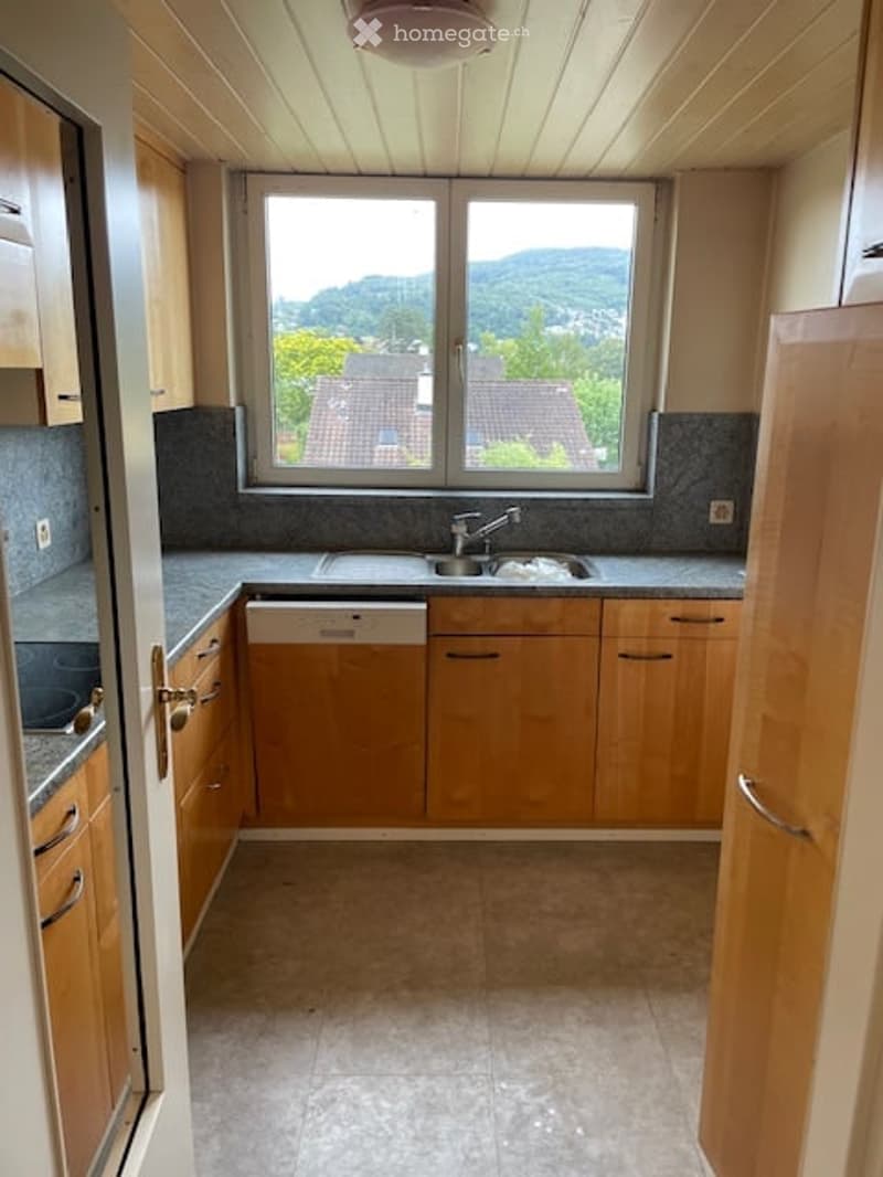 Bright kitchen with wooden cabinets, granite countertops, and a large window offering a scenic view of the surrounding landscape.