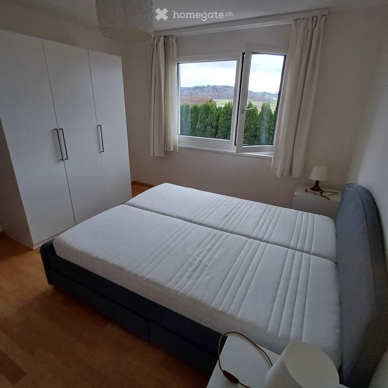 Bedroom. A well-lit bedroom with a large double bed, a wardrobe, a nightstand with a lamp, and large windows offering a scenic view.