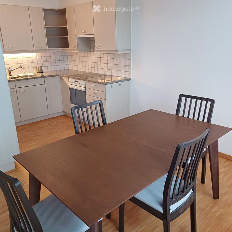 Kitchen. Modern kitchen with light grey cabinets, a dark wooden dining table with four chairs, and a built-in oven. The kitchen features a granite countertop and a sink with a faucet.