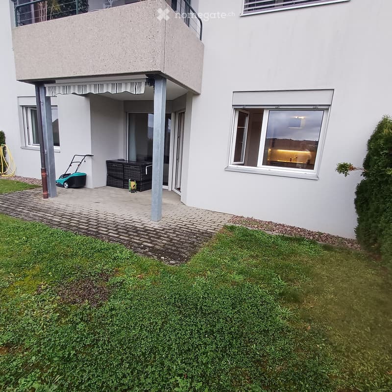 Garden / Outdoor Area. Garden area with a well-maintained lawn, a paved pathway, and a small patio with outdoor furniture and a lawnmower.
