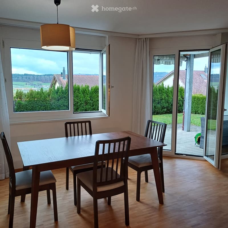 Furnished Room. Bright dining room with wooden floor, large windows, and a view of the countryside. A modern dining table with four chairs is placed near the window.