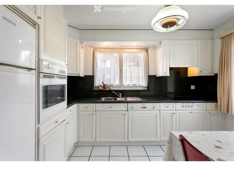 Modern kitchen with white cabinets, black countertops, stainless steel appliances, and a small dining area with a table and chair.