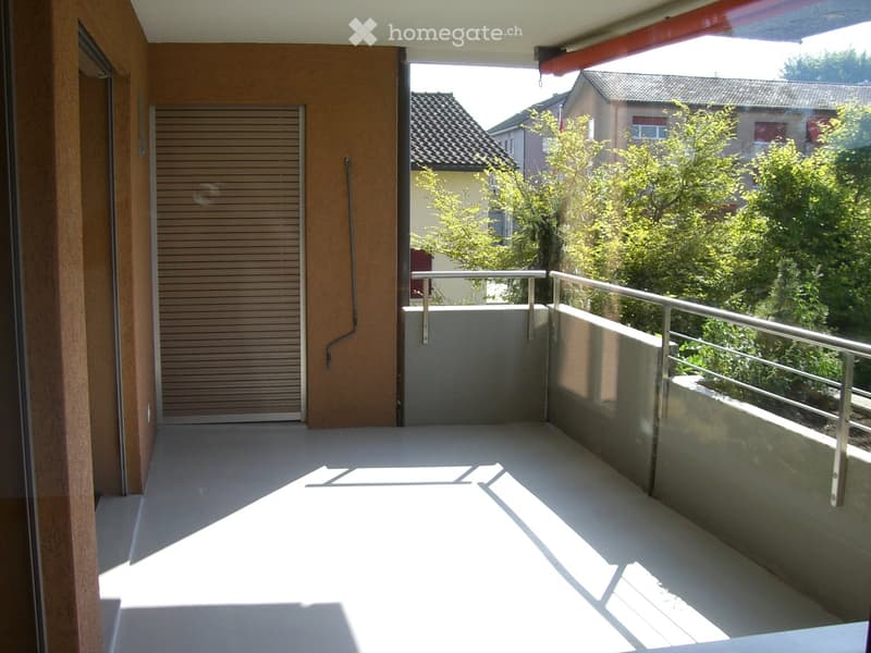 Balcony with metal railing, concrete floor, and view of neighboring houses and greenery.