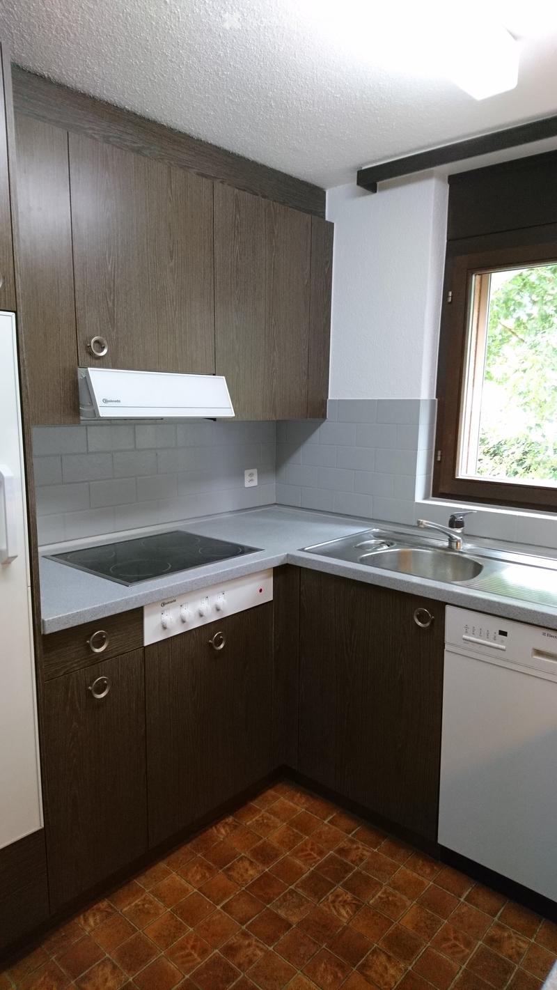 Modern kitchen with dark wood cabinets, stainless steel sink, electric stove, dishwasher, and range hood. Light grey tiled backsplash and brown tiled floor.